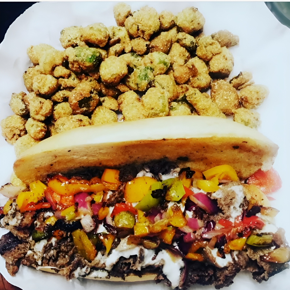 A Big Easy Bistro cheesesteak with colorful peppers and onions, served with fried okra.