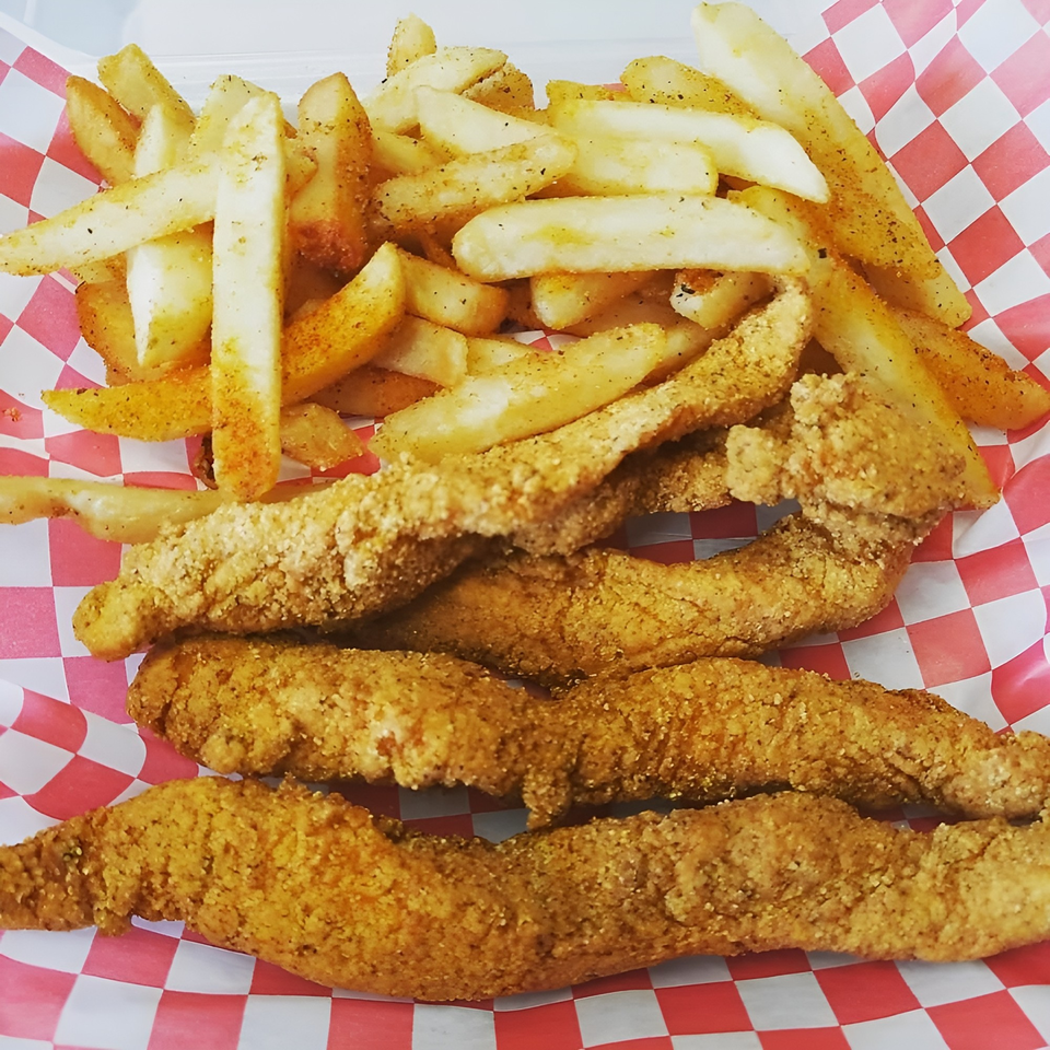 Crispy fried chicken tenders and seasoned french fries in a red and white checkered basket.